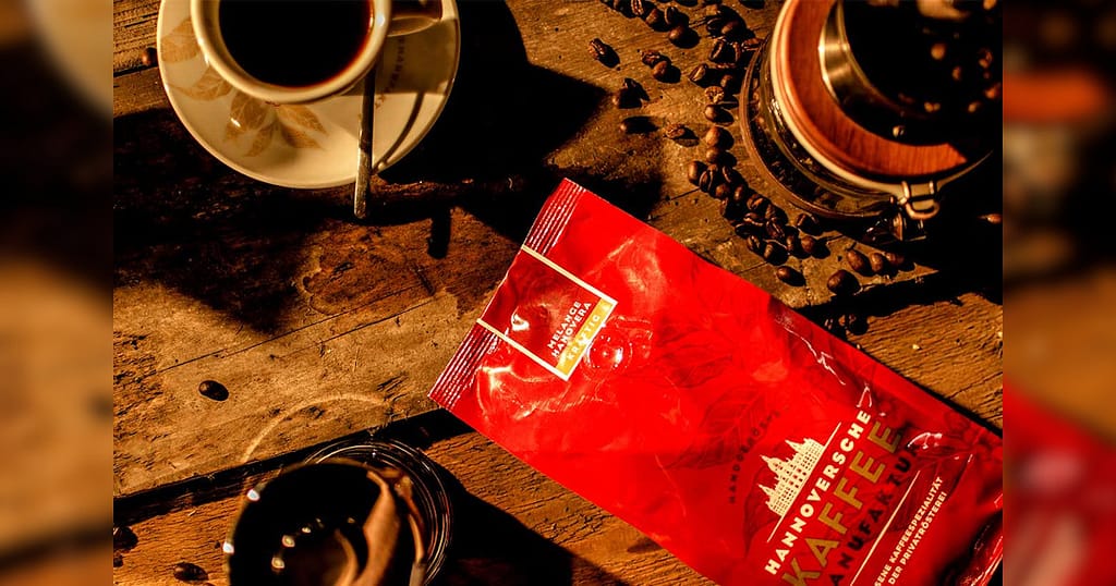 Rote Tüte für Kaffeebohnen der Hannoverschen Kaffeemanufaktur liegt auf einem Holztisch.